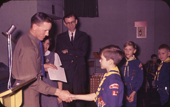 David gets a cub scout handshake as dad & mom look on